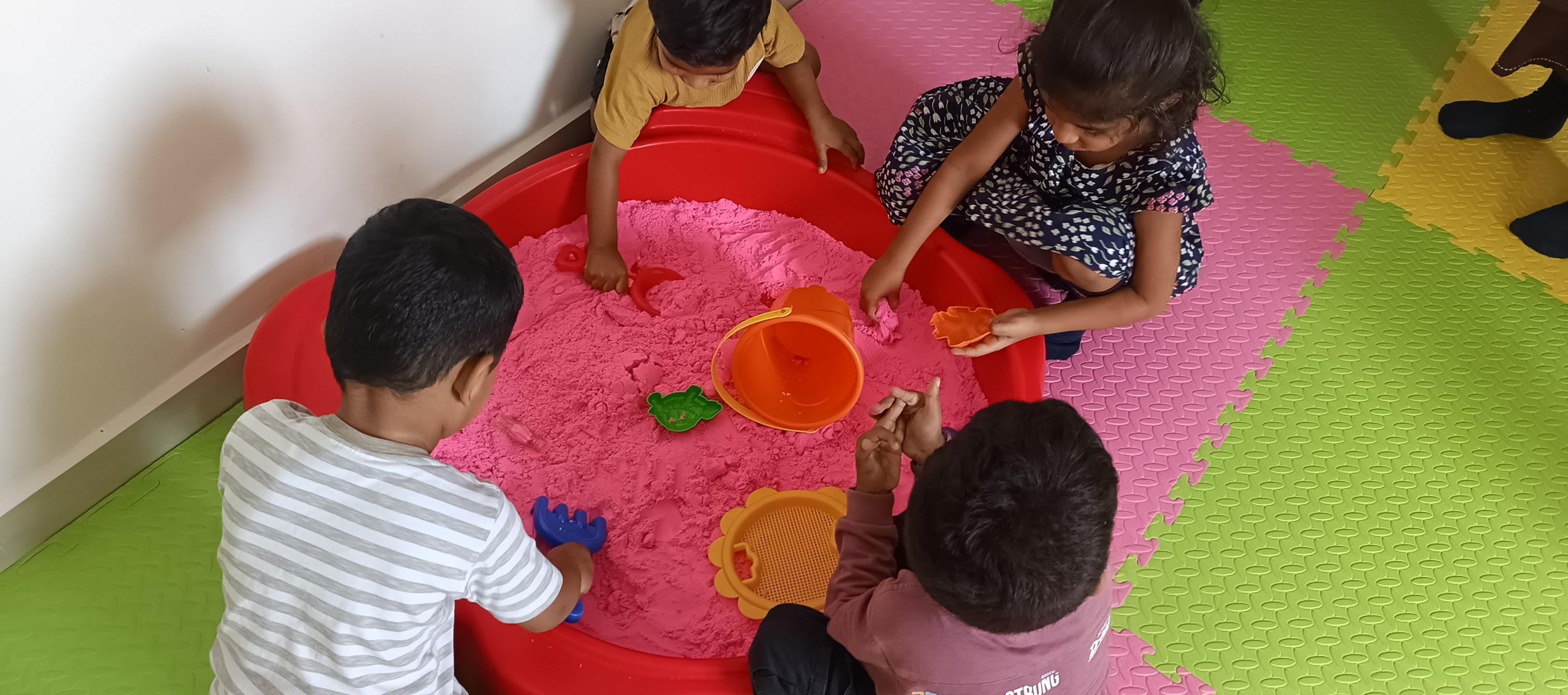 Children playing with pink sensory sand tub and tools